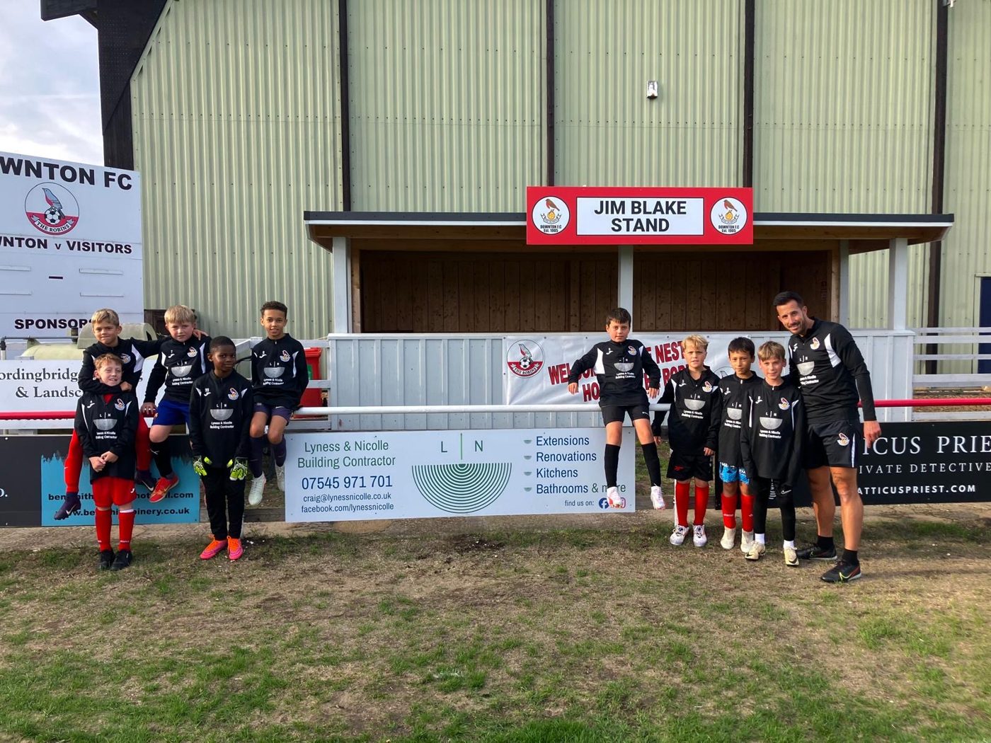 Downton FC youth players and coach in Lyness & Nicolle sponsored training tops beside the Lyness & Nicolle pitch-side sign